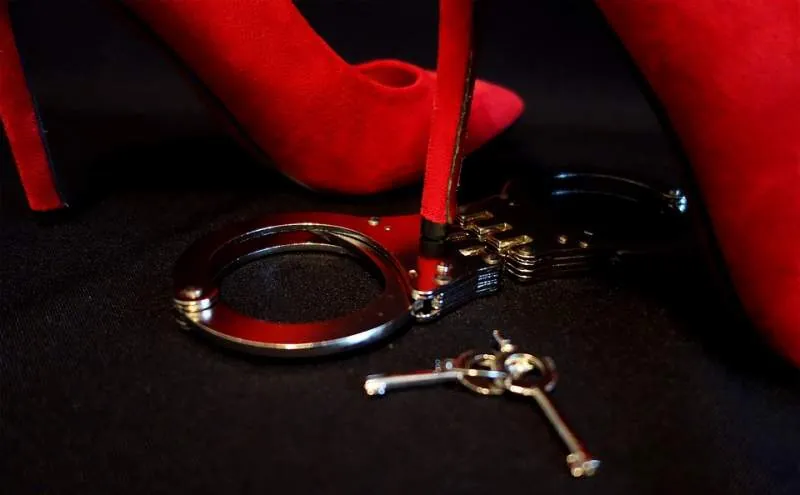 Rote High Heels, Handschellen und Schlüssel auf schwarzem Untergrund